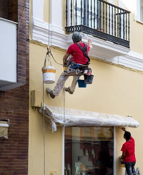 pintores colgados realizando trabajos en fachada